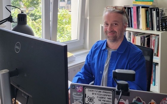 Robin Berjon, a digital governance specialist, smiles at the camera as he sits at his computer in his home office.
