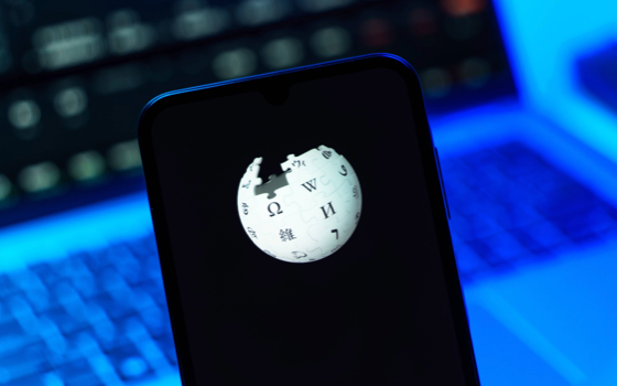The Wikipedia puzzle-globe logo on a phone screen in front of a laptop lit in blue