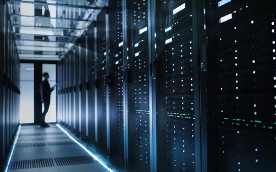 A person walking between rows of server racks in a dimly lit data centre.